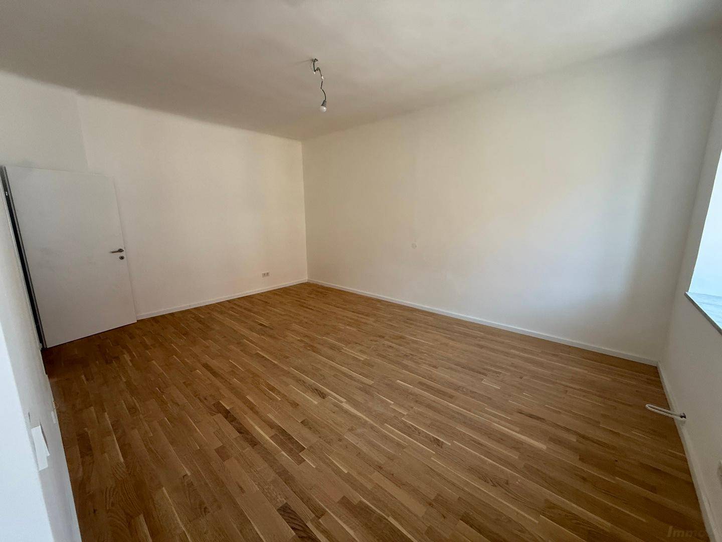 Leeres Zimmer mit warmem Parkettboden und viel Tageslicht, bereit für neue Bewohner.