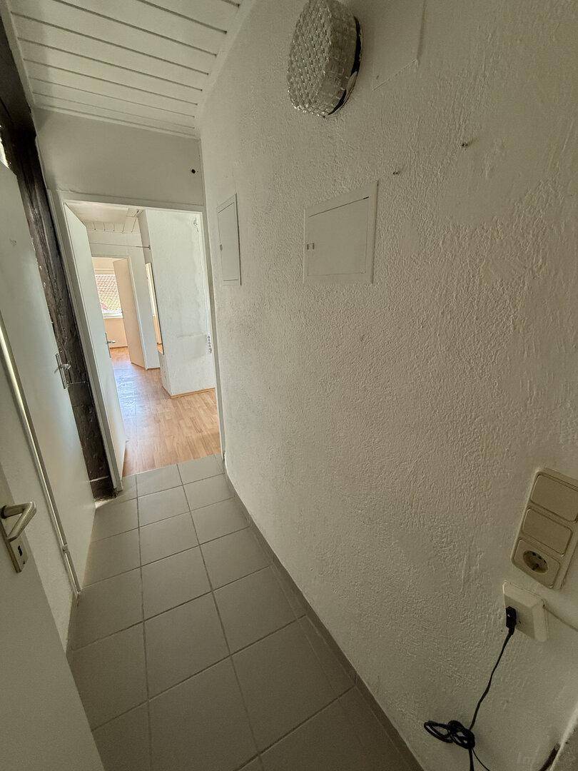 Schmaler Flur mit hellen Fliesen und strukturierten Wänden, der zu weiteren Räumen führt.