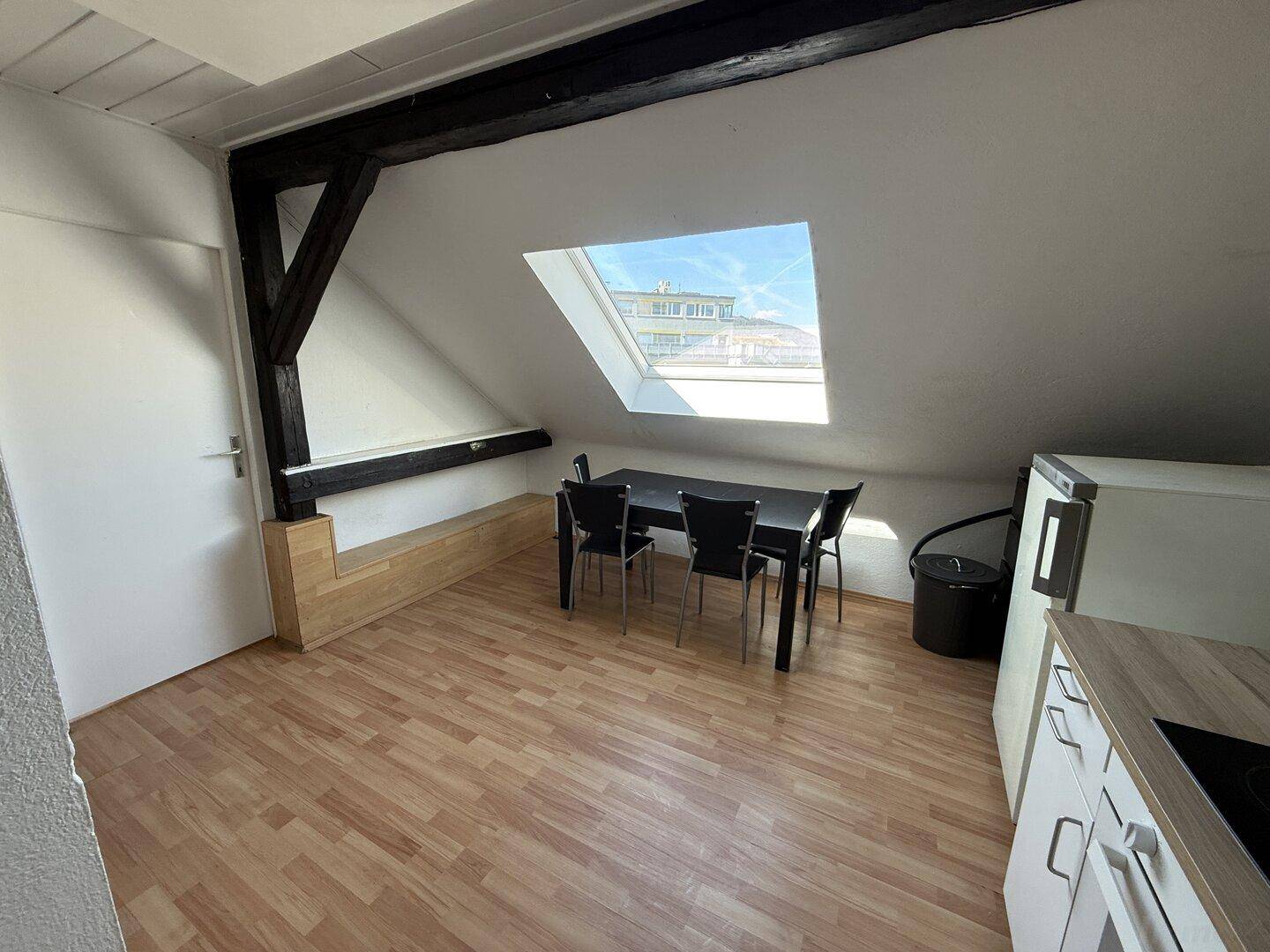 Gemütlicher Essbereich im Dachgeschoss mit Holzbalken, Dachfenster und integrierter Sitzbank.