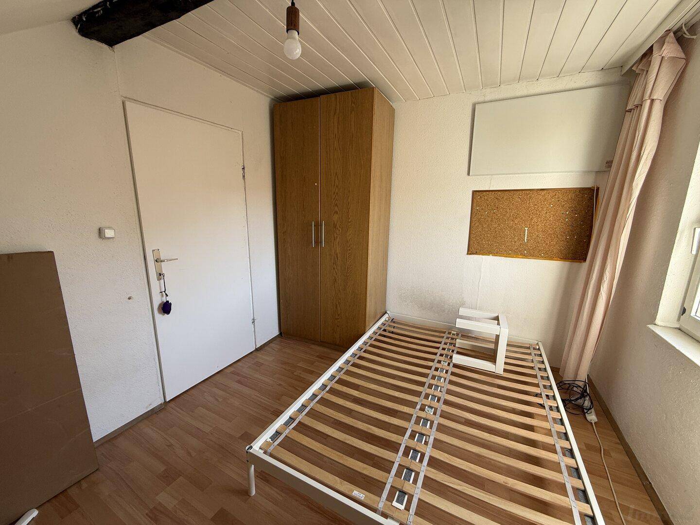 Schlafzimmer im Dachgeschoss mit Bettrahmen, Kleiderschrank und Fenster.