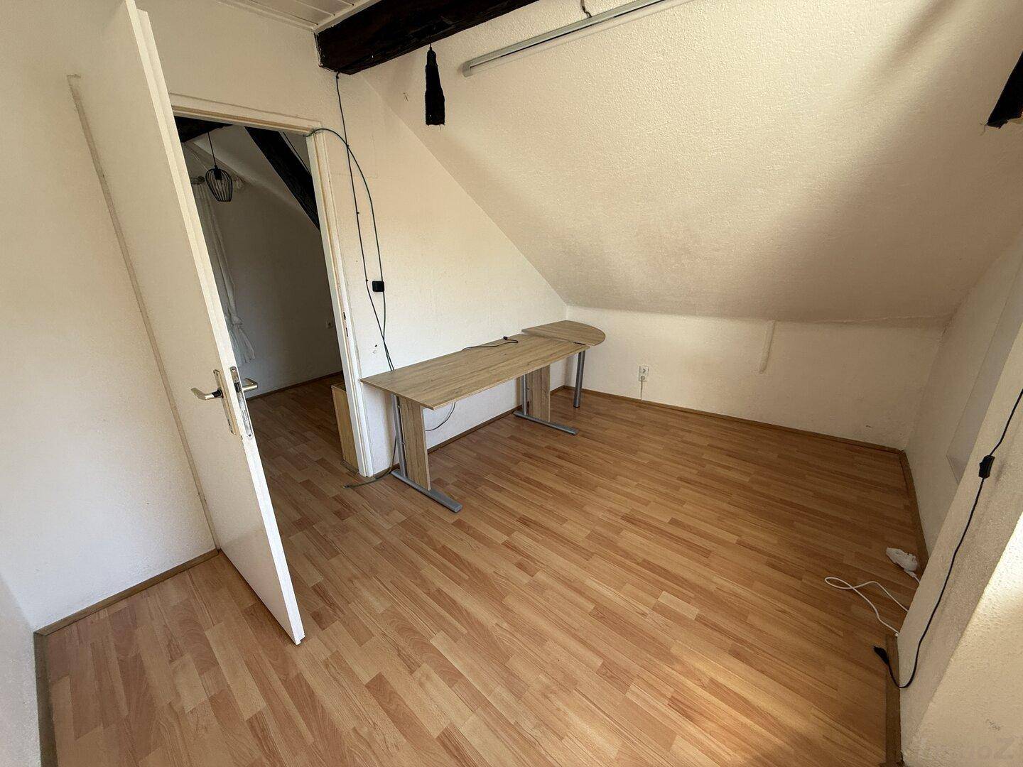 Dachzimmer mit Laminatboden und Schreibtisch, bietet Zugang zu weiteren Räumen.