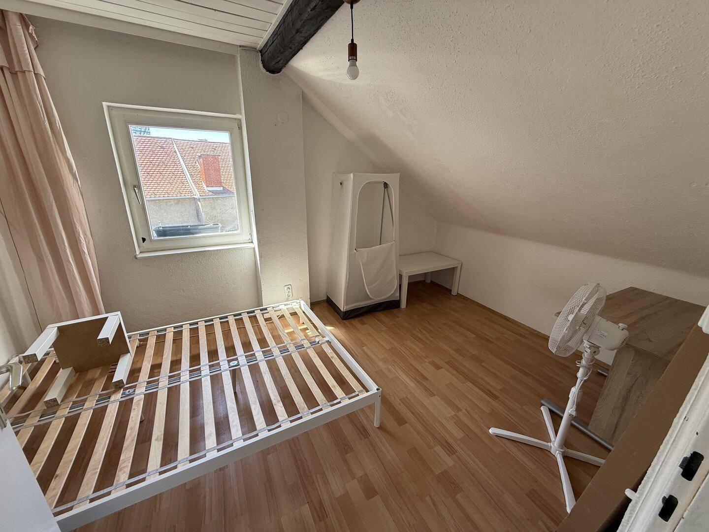 Schlafzimmer im Dachgeschoss mit Bettrahmen, Fenster und Dachschräge, hell und funktional.