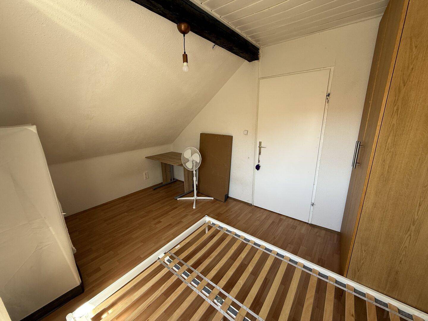 Dachgeschoss-Schlafzimmer mit Bettrahmen, Dachschräge und Ventilator für angenehmes Klima.
