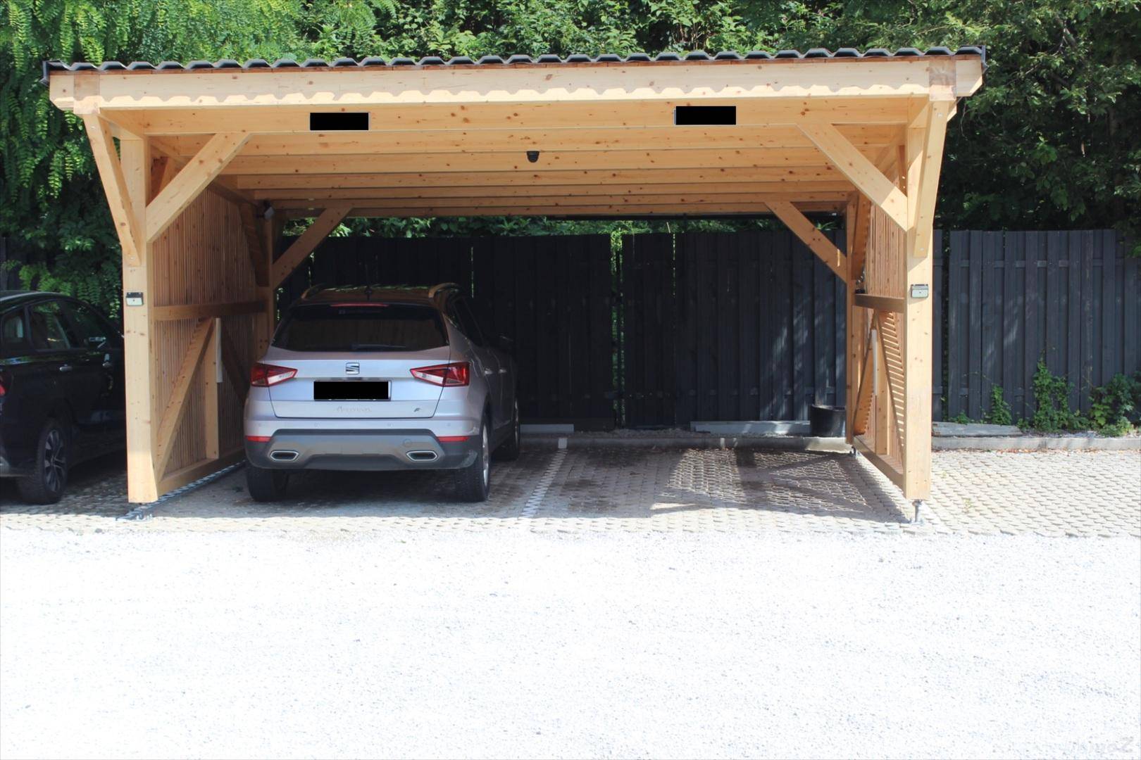 Nahaufnahme des stabilen Holzcarports mit einem geparkten Fahrzeug und blick auf den Zaun.