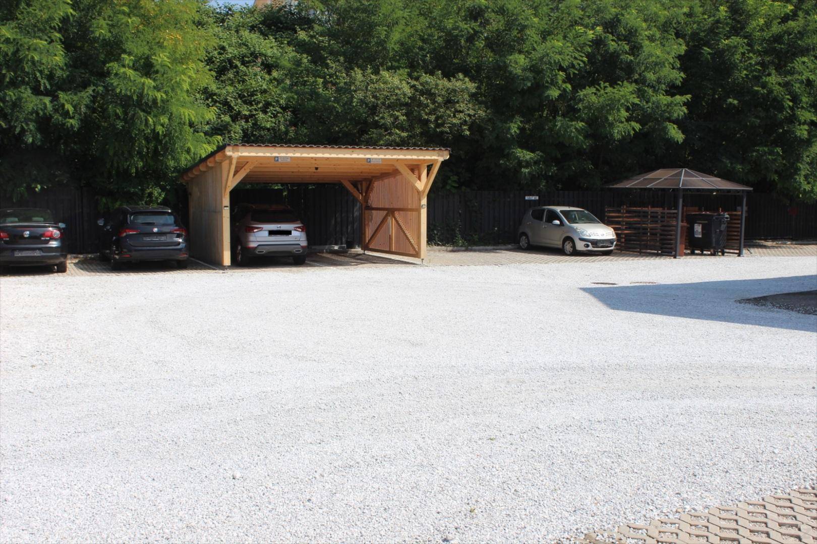 Geräumiger Außenbereich mit Holzcarport und mehreren Stellplätzen, umgeben von Bäumen.