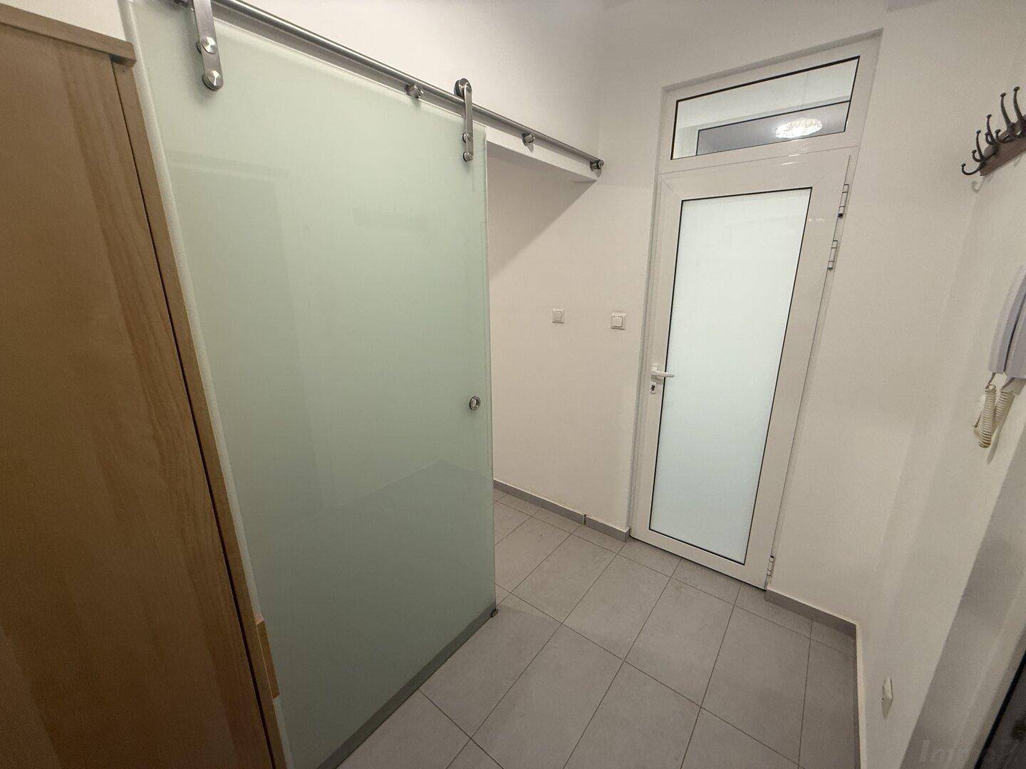Heller Flur mit Fliesenboden, einem Holzschrank und einer modernen Schiebetür aus Milchglas.