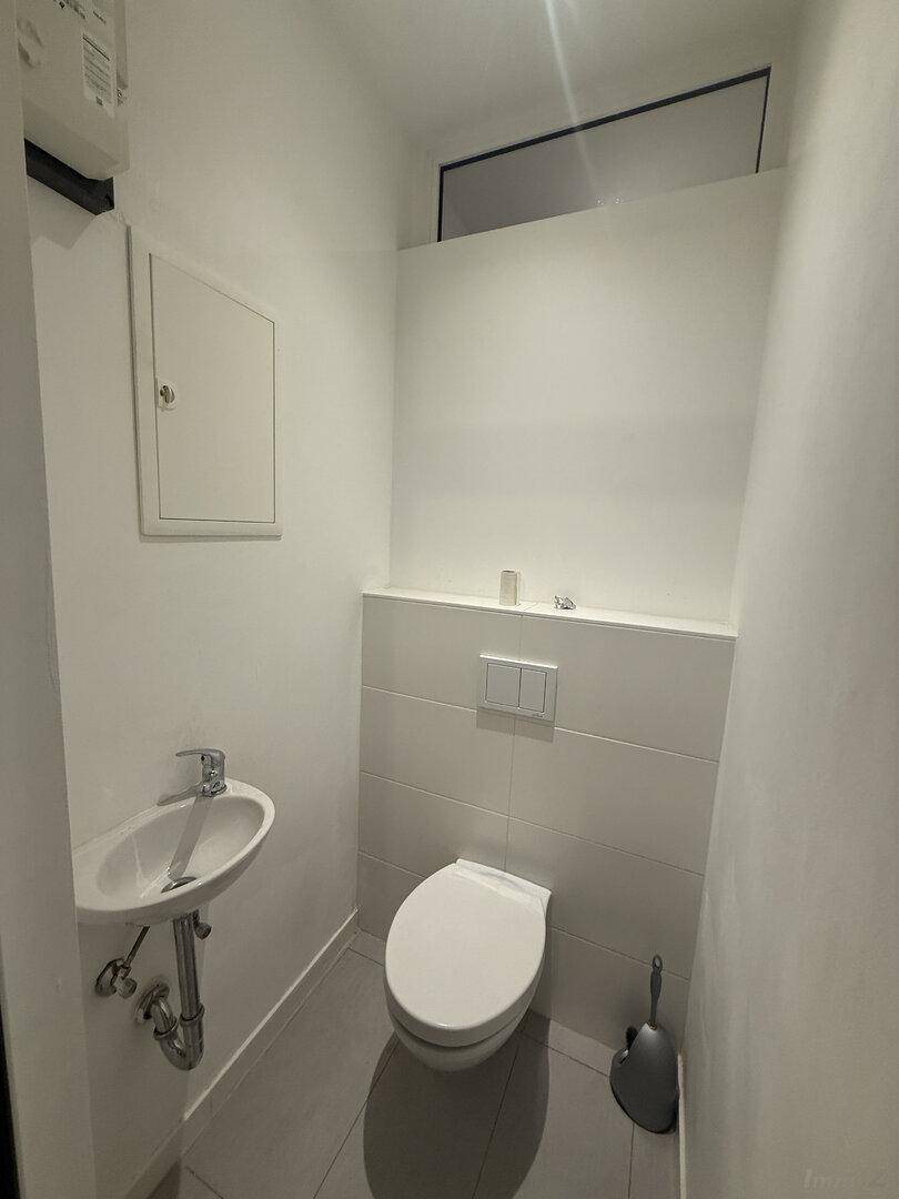 Kleines Gäste-WC mit wandhängendem WC, Waschbecken und einem Fenster für Tageslicht.