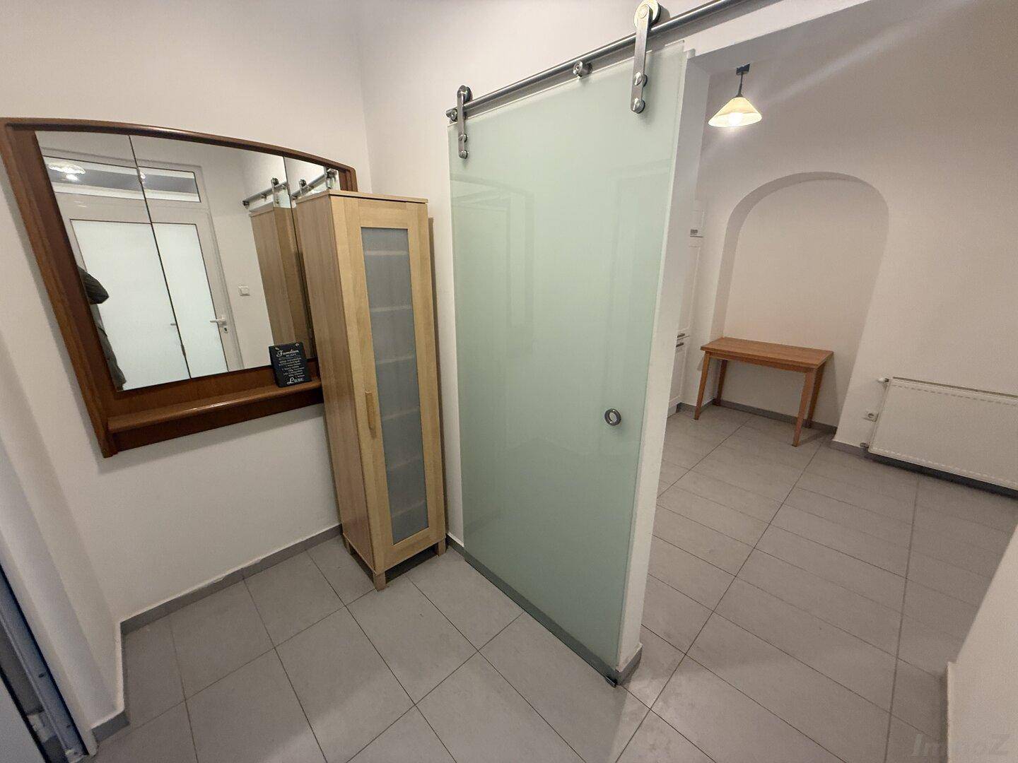 Eingangsbereich mit Fliesenboden, einem Spiegel, Holzschrank und einer modernen Schiebetür aus Milchglas.