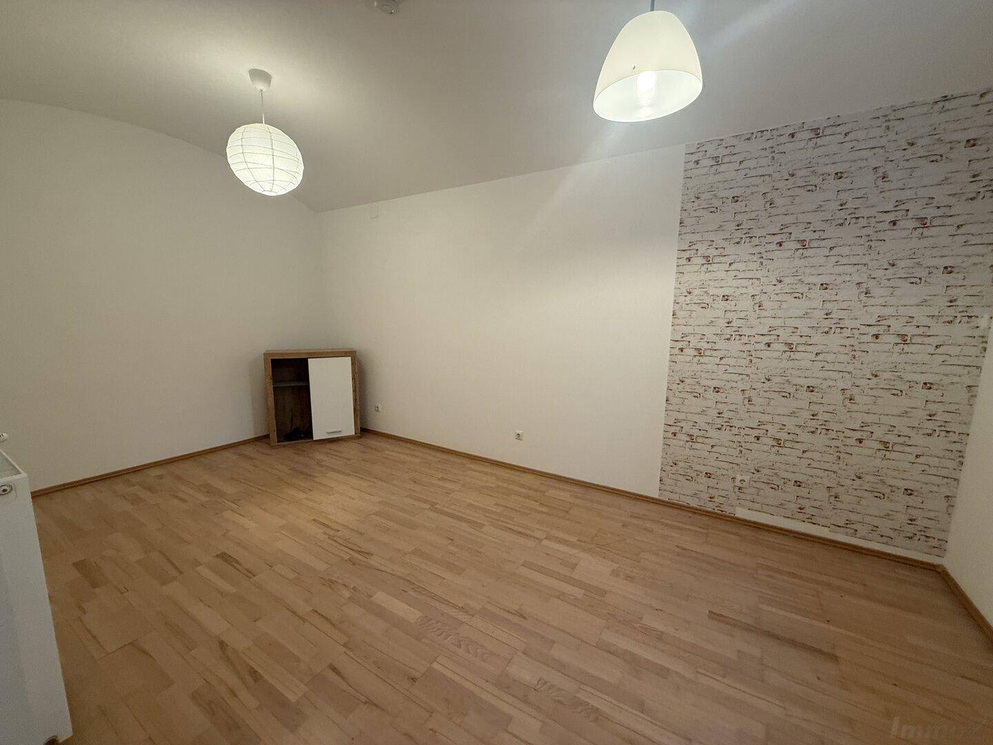 Geräumiges Zimmer mit Holzfußboden und einer Akzentwand in Ziegelsteinoptik, hell beleuchtet.