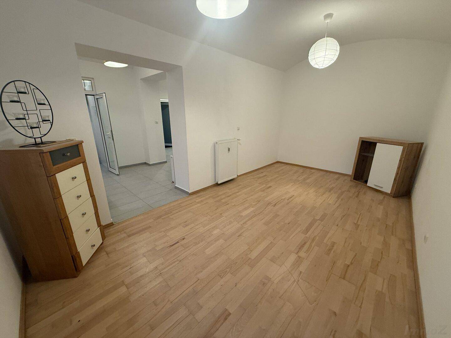 Heller Raum mit Holzfußboden und Blick in den angrenzenden, gefliesten Flurbereich.