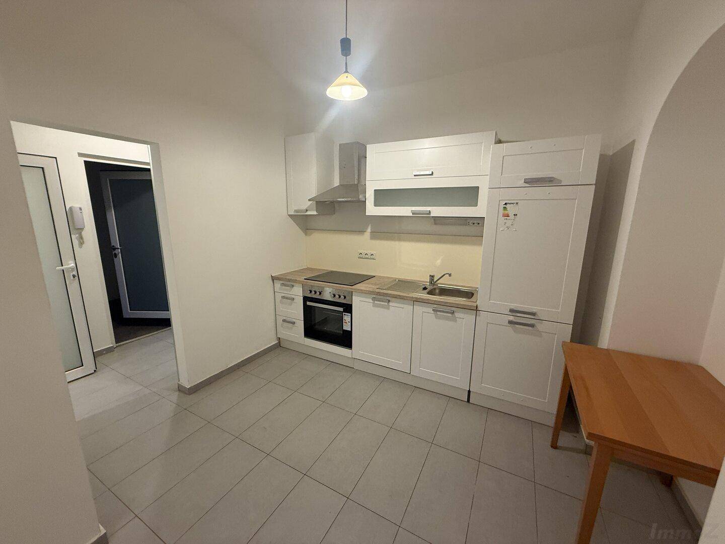 Kompakte Einbauküche mit weißen Fronten, Kochfeld, Backofen und Kühlschrank, praktisch eingerichtet.
