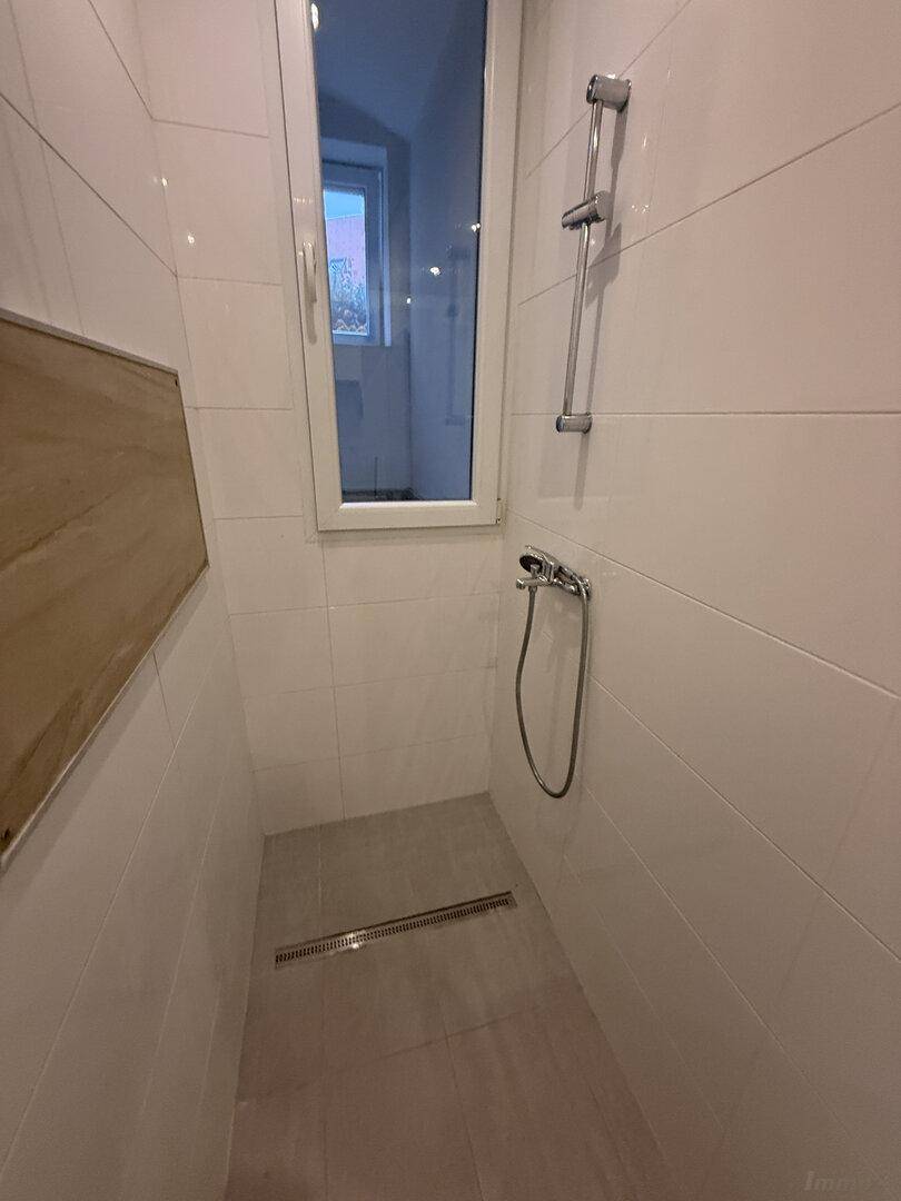 Ebenerdige Dusche im modernen Badezimmer mit weißen Fliesen und einem hohen Fenster.