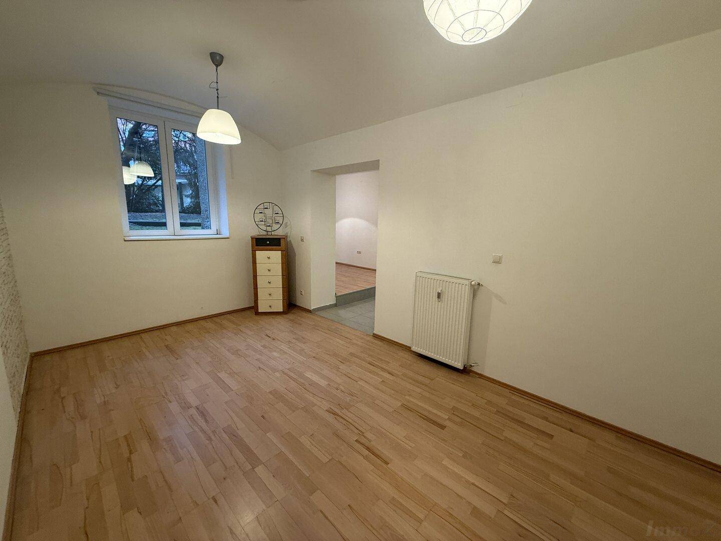 Freundliches Zimmer mit Holzfußboden, Fenster und Heizkörper, bereit zur individuellen Gestaltung.