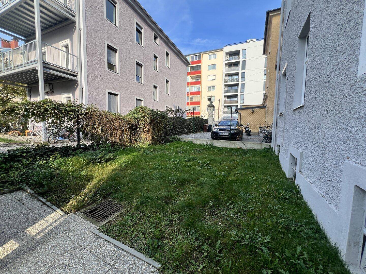Blick auf eine grüne Fläche im Innenhof, umgeben von Wohngebäuden mit Balkonen und einem geparkten Fahrzeug.