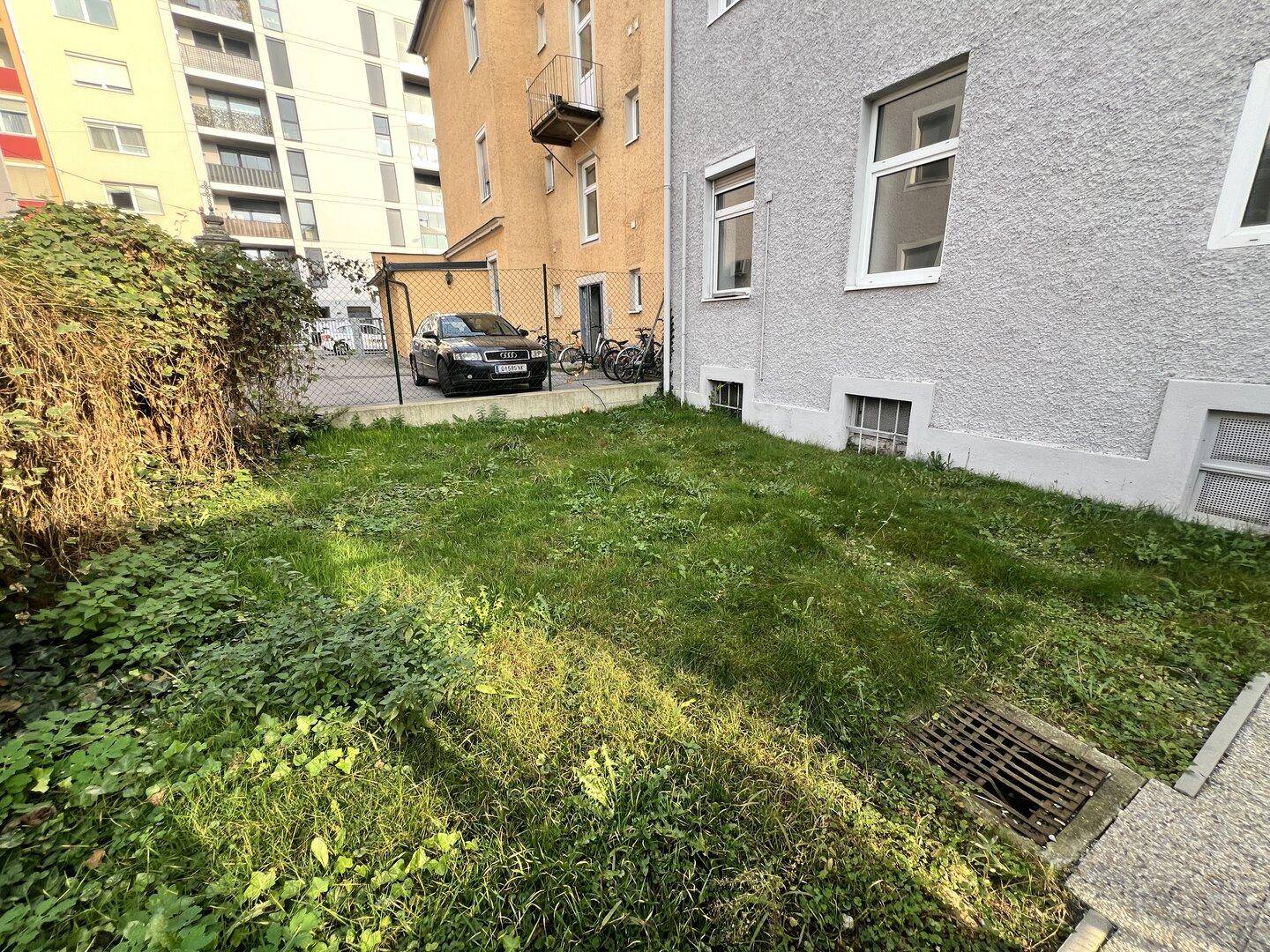 Grünfläche zwischen Gebäuden mit einem geparkten Auto im Hintergrund und angrenzenden Wohnungen.
