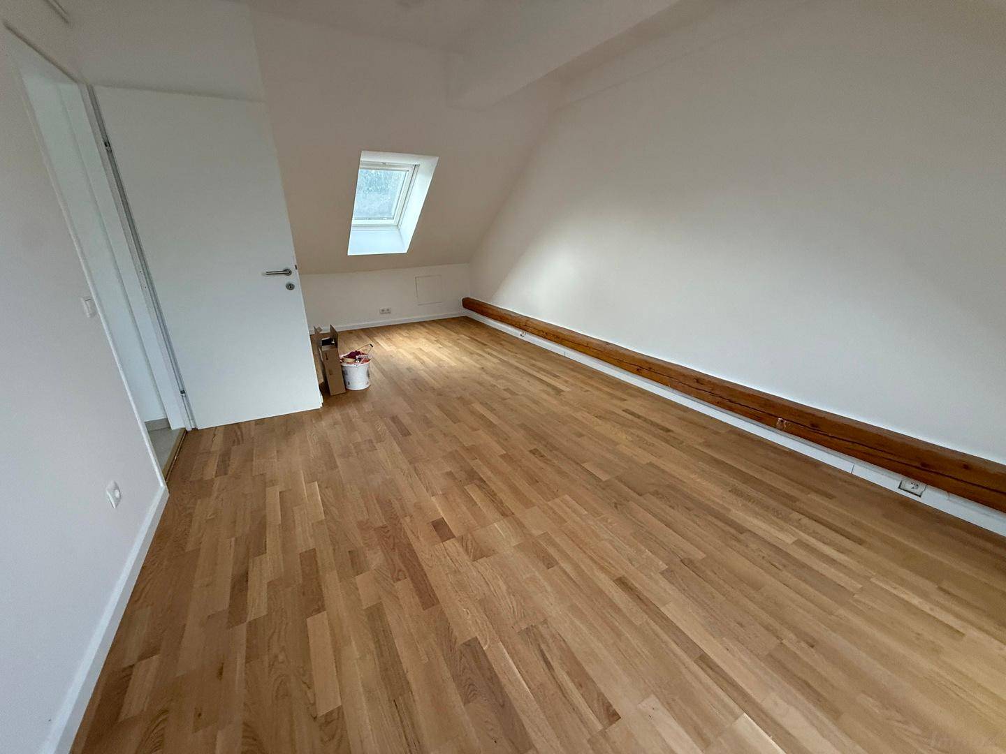 Helles Schlafzimmer im Dachgeschoss mit Holzboden, Dachfenster und sichtbarem Holzbalken.