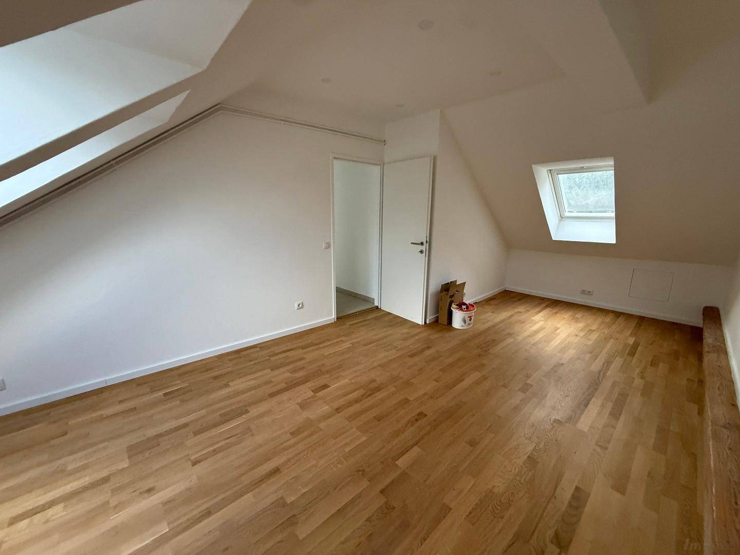 Helles Dachgeschosszimmer mit Holzboden, schrägen Wänden und mehreren Dachfenstern für viel Licht.