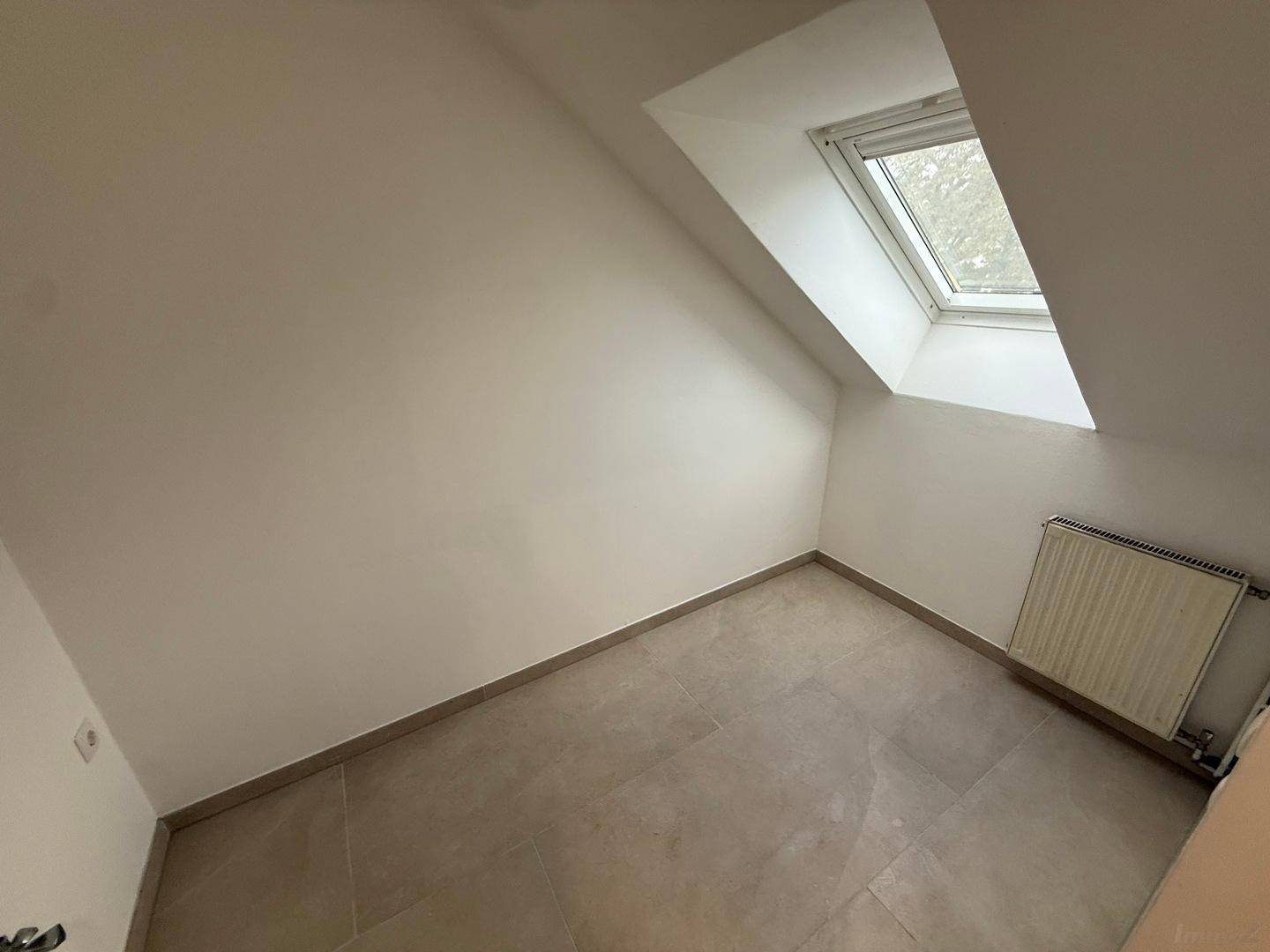 Kleiner Raum im Dachgeschoss mit Fliesenboden, Heizkörper und Dachfenster.