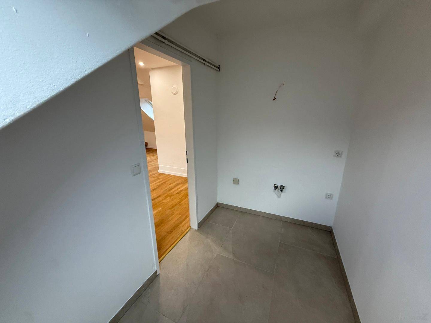 Kleiner Hauswirtschaftsraum mit Fliesenboden und Anschlüssen für Waschmaschine.