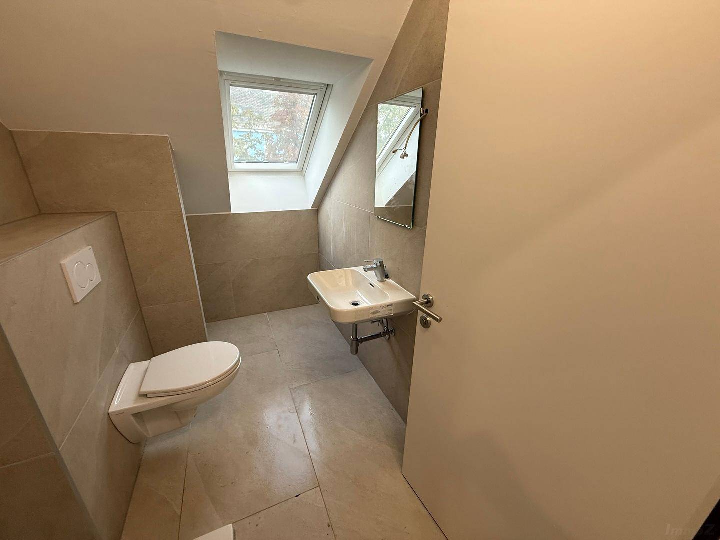 Helles Badezimmer mit WC, Waschbecken, Spiegel und Dachfenster.