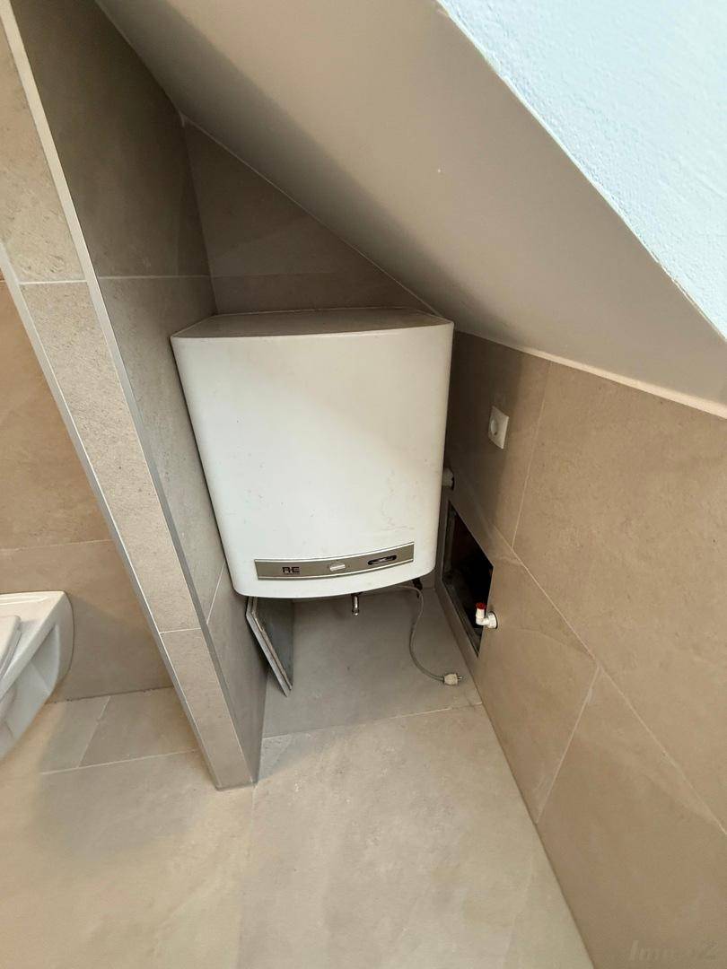 Warmwasserbereiter in einem gefliesten Bereich unter einer Dachschräge, effizient installiert.