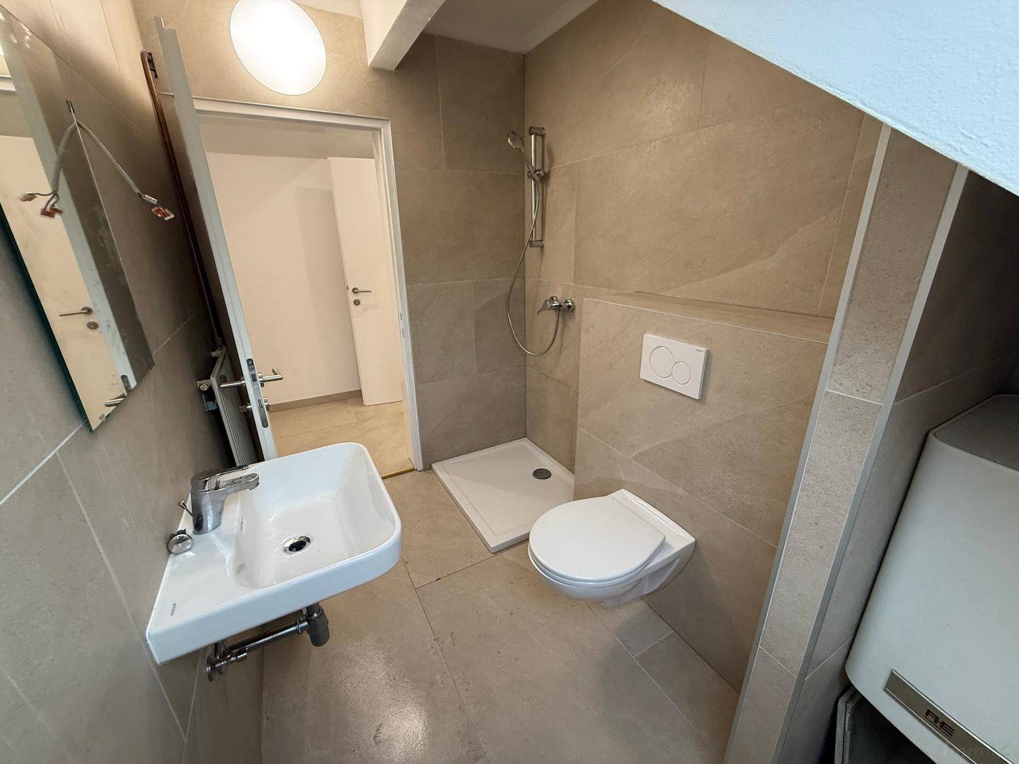 Funktionales Badezimmer mit Dusche, WC, Waschbecken und Warmwasserbereiter unter der Dachschräge.