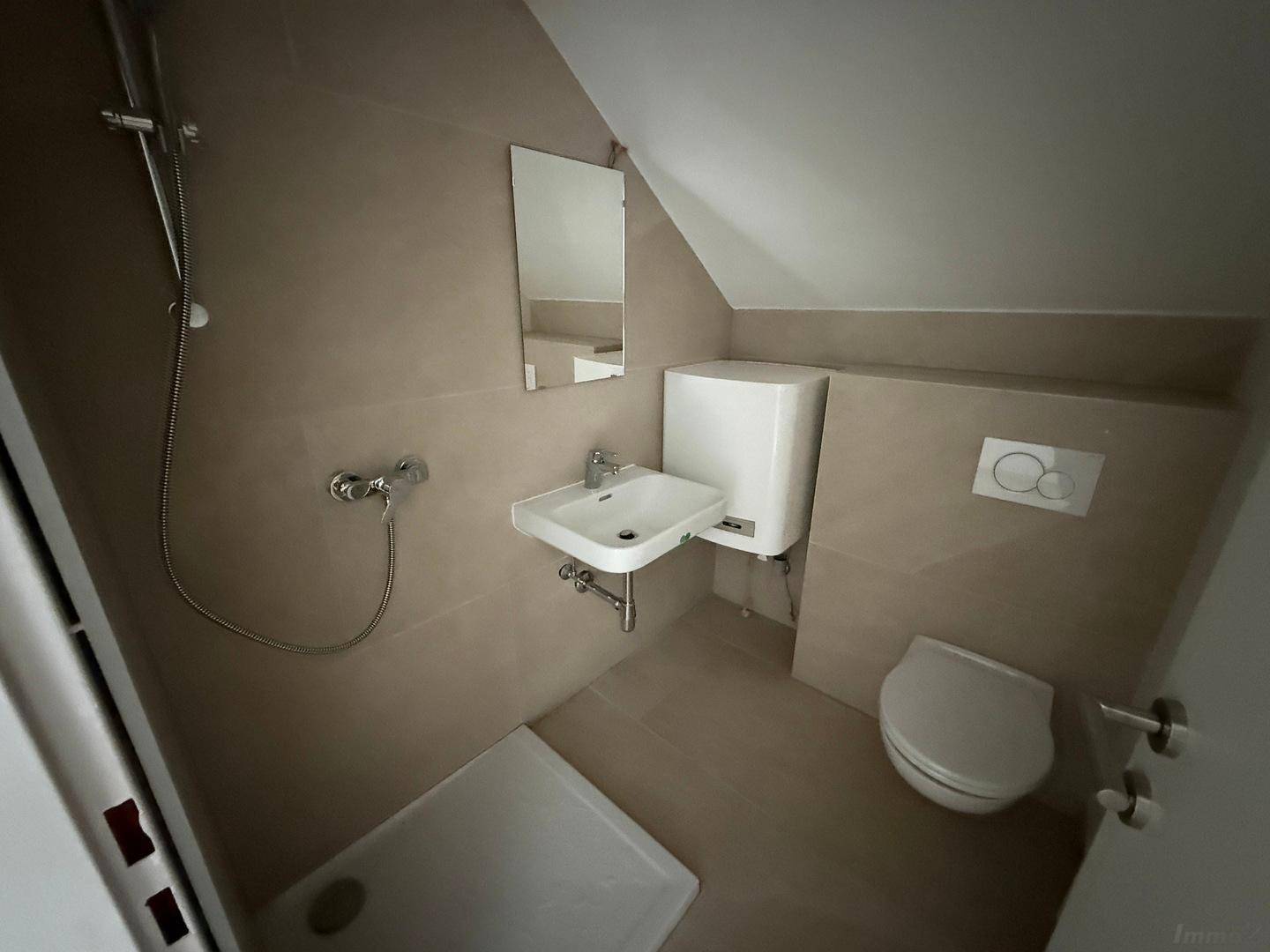 Modernes Badezimmer im Dachgeschoss mit Dusche, WC und Waschbecken, komplett gefliest.