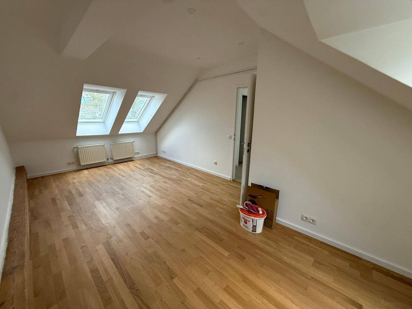 Großes Dachzimmer mit zwei Dachfenstern, Parkettboden und Heizkörpern, bietet viel natürliches Licht.