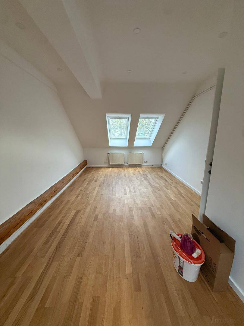 Weitläufiges Dachzimmer mit Parkettboden, Dachschrägen und zwei hellen Dachfenstern, sehr einladend.