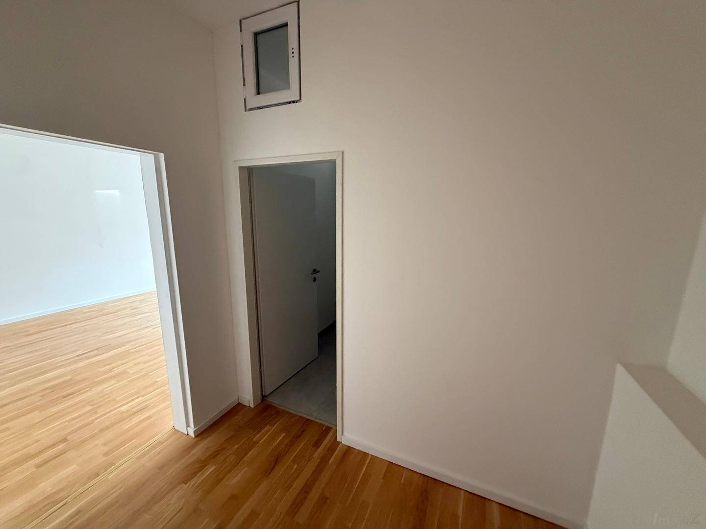 Heller Flur mit Holzboden und Zugang zu weiteren Räumen, inklusive eines kleinen Fensters.