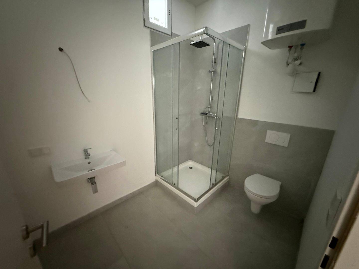 Modernes Badezimmer mit Duschkabine, WC, Waschbecken und einem kleinen Fenster.