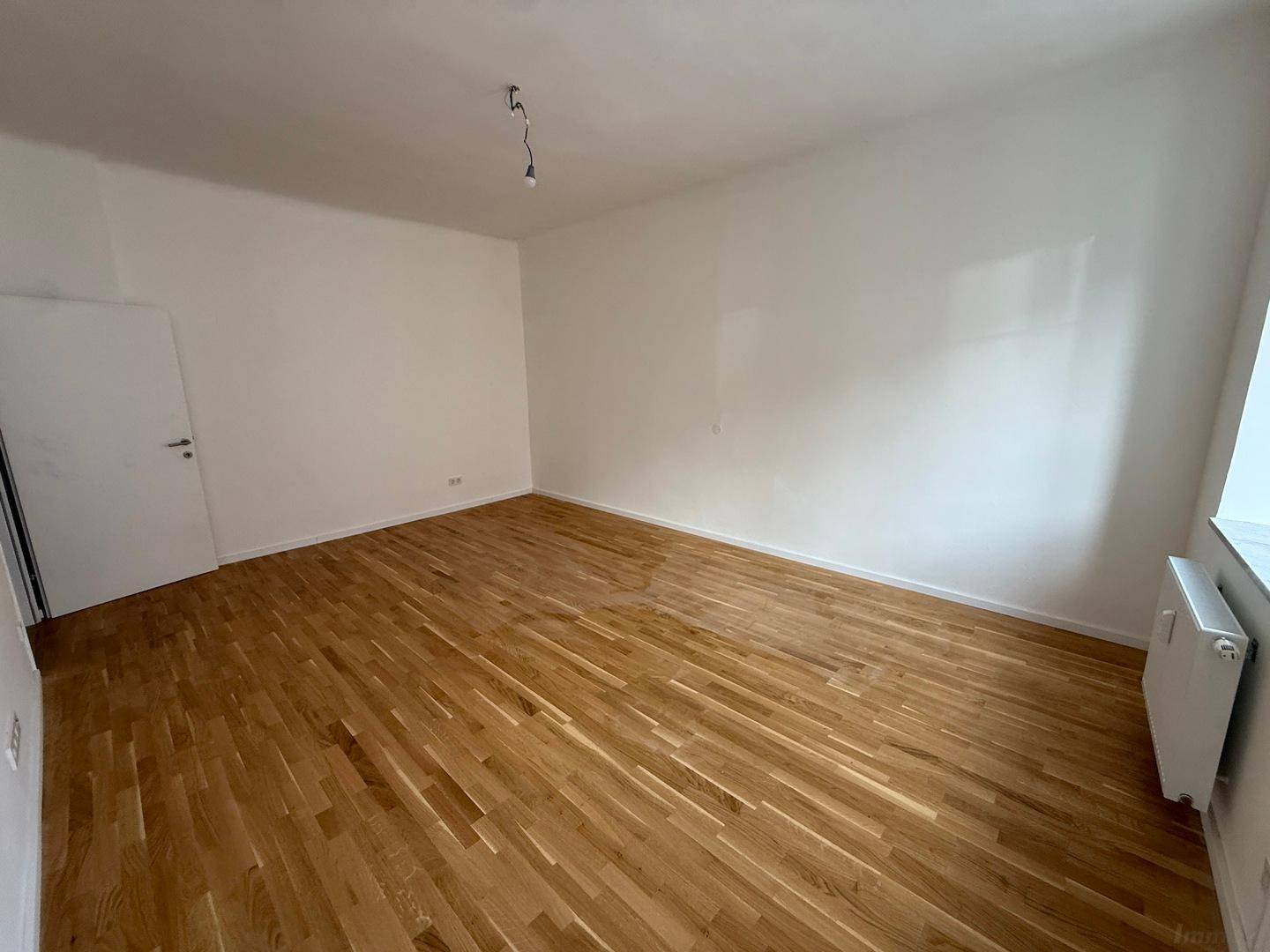 Ruhiges Zimmer mit Holzboden, weißen Wänden und einem Fenster für natürliches Licht.