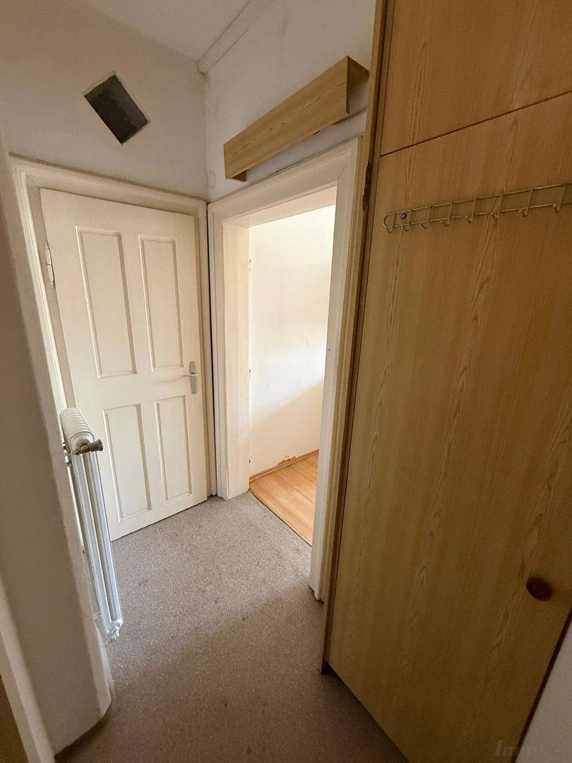 Schmaler Flur mit Teppichboden, einer Holztür und einem einfachen Einbauschrank.