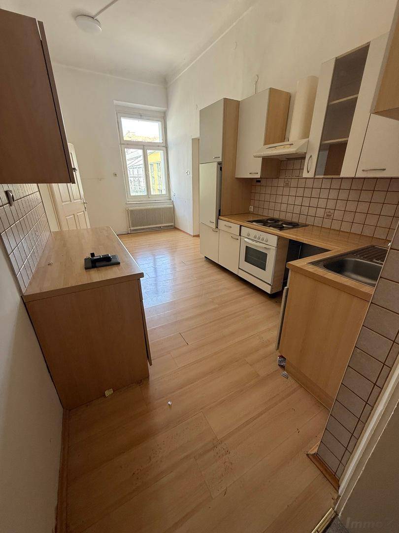 Helle Küche mit Holzschränken, Herd, Spüle und einem Fenster, das viel Tageslicht hereinlässt.
