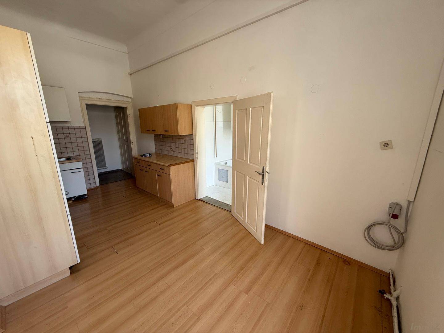 Küche mit Holzboden und einer offenen Tür, die den Blick in ein weiß gefliestes Badezimmer freigibt.