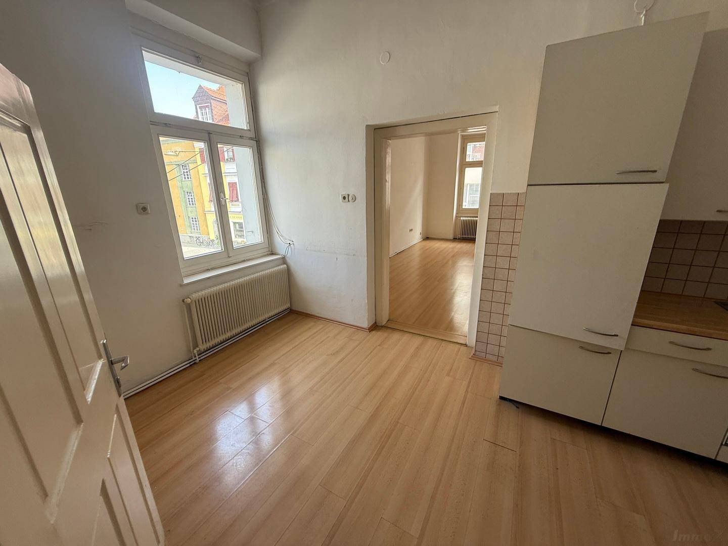 Heller Raum mit Holzboden, Fenster und angedeuteter Küchenzeile, ideal als Essküche.