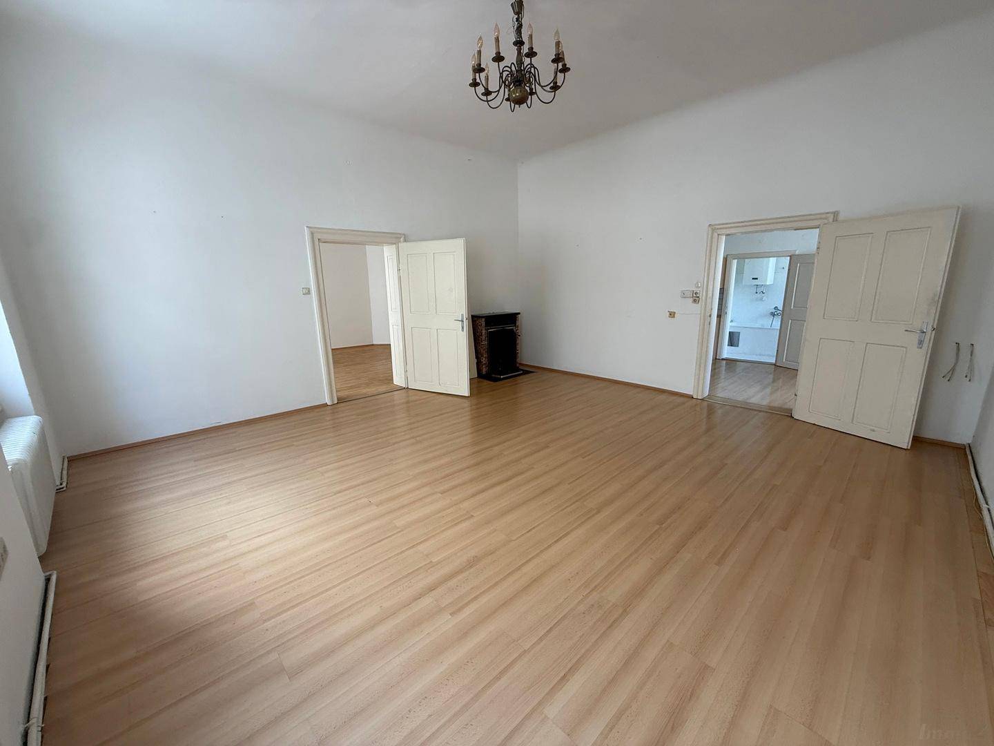 Großes Zimmer mit Holzboden, weißen Wänden und mehreren offenen Türen zu angrenzenden Räumen.