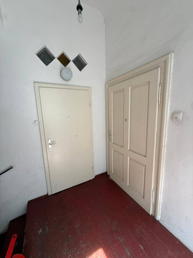 Eingangsbereich mit zwei Türen, weißen Wänden und einem dunklen, rotbraunen Holzboden.