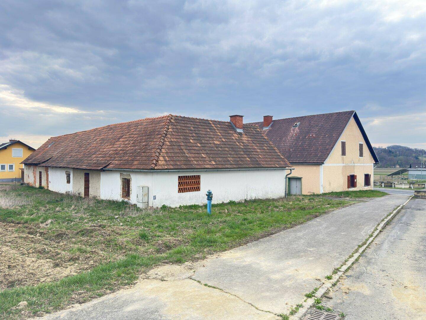 Gesamtansicht des Hauptgebäudes und des Nebengebäudes mit Zufahrtsweg und angrenzenden Feldern.