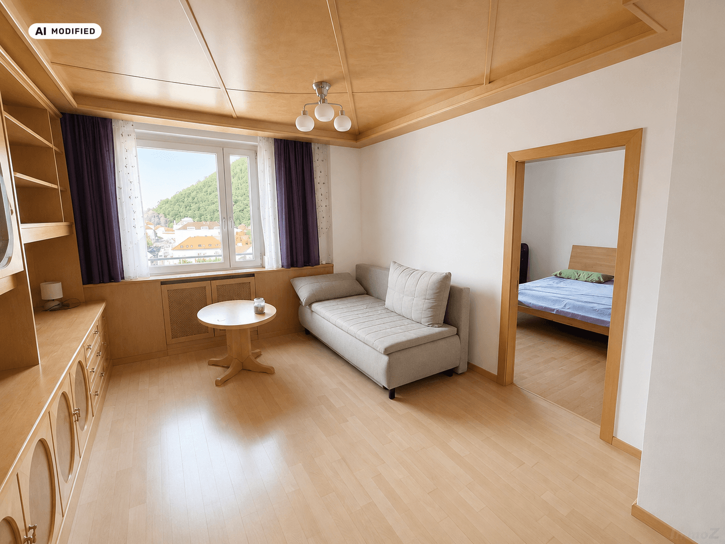Helles Wohnzimmer mit bequemer Couch, kleinem Tisch und Zugang zum Schlafzimmer.