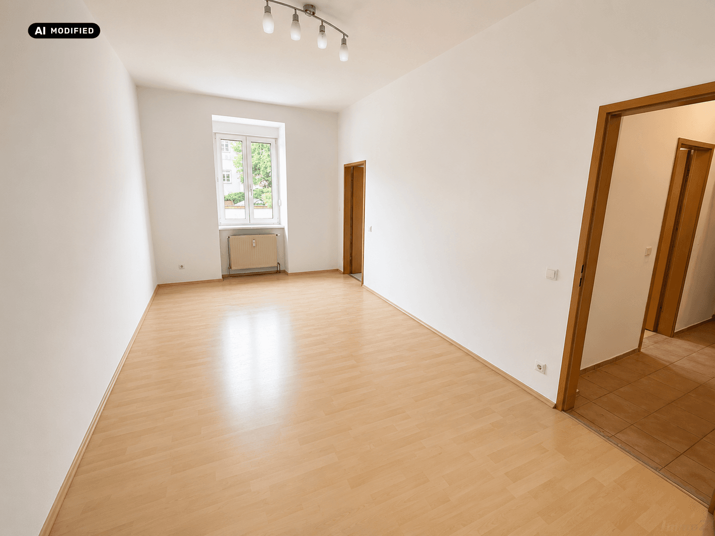 Geräumiges Wohnzimmer mit hellem Laminatboden und einem Fenster mit Blick ins Grüne.