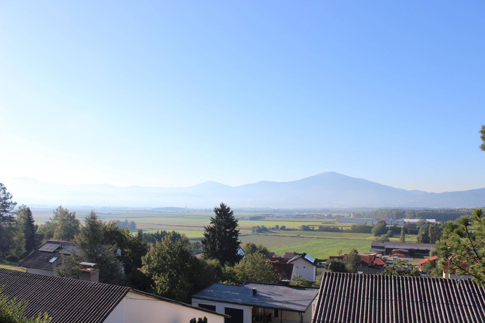 Weitläufiger Blick über ein Tal mit Feldern und einer beeindruckenden Bergkulisse am Horizont.