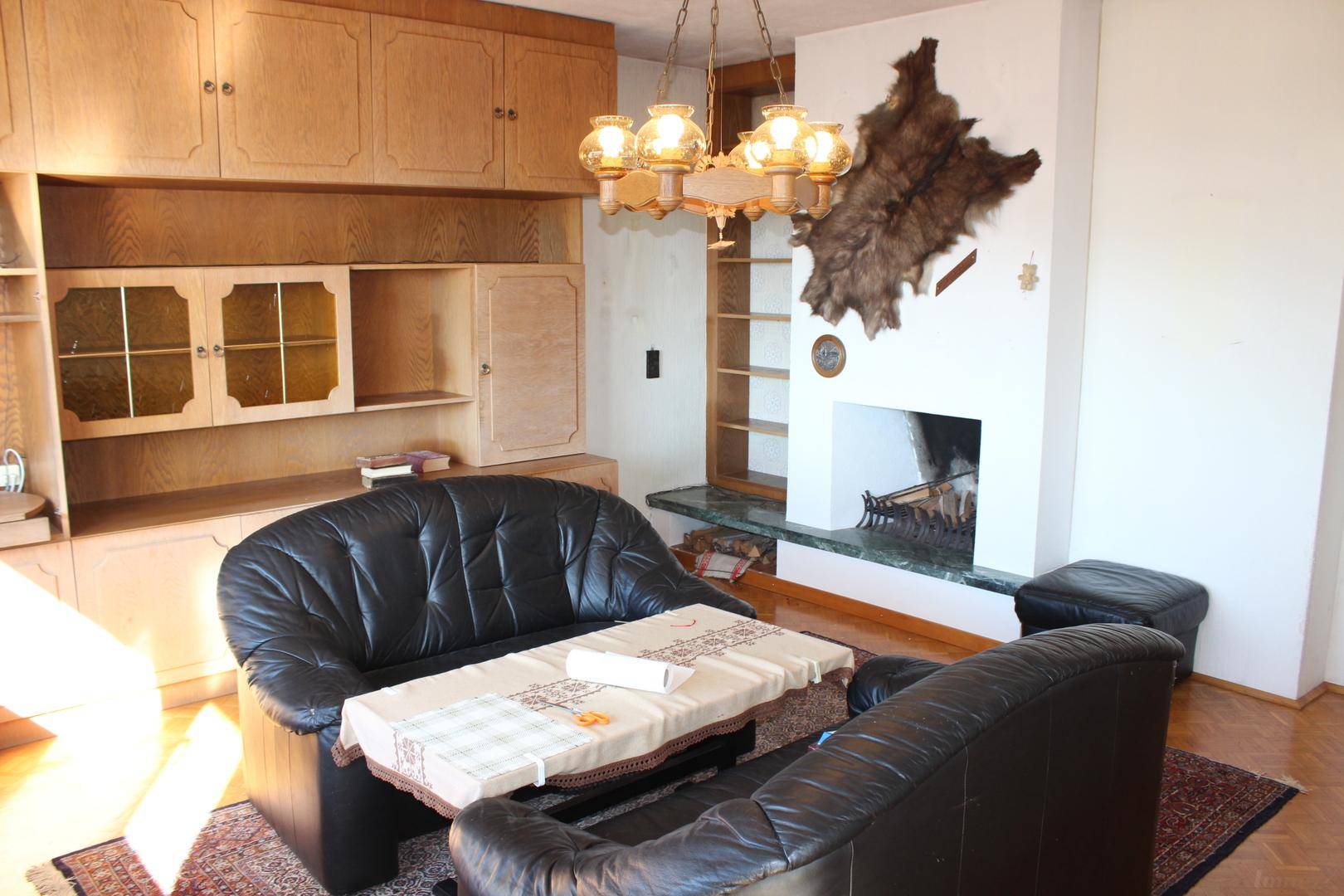 Wohnzimmer mit Kamin, Holzschrankwand und rustikaler Fell-Dekoration an der Wand.