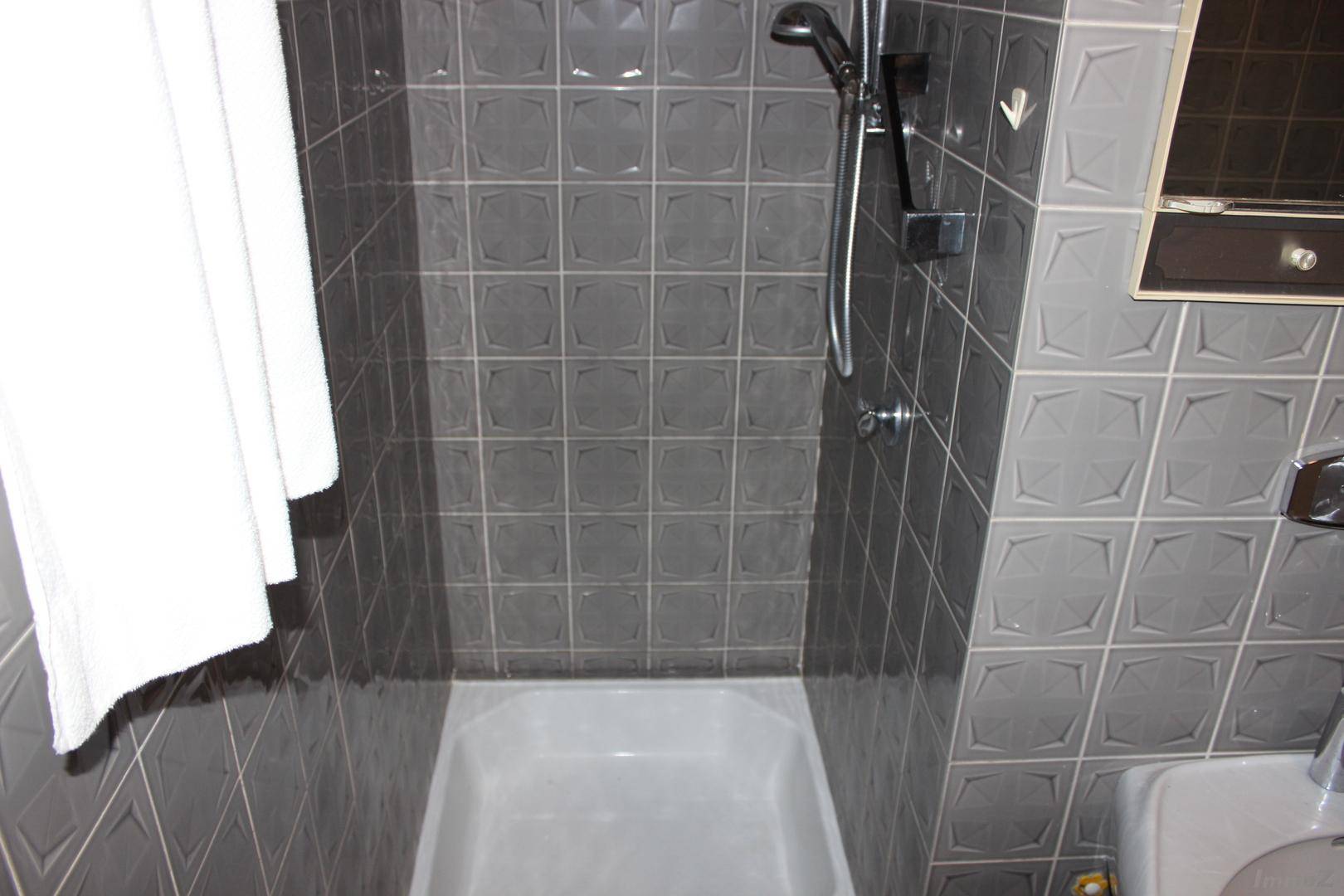 Duschbereich im Badezimmer mit grauen Fliesen und einer Duschwanne, funktional und einfach.