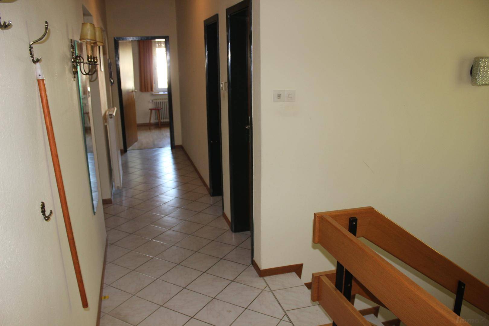 Heller Flur mit Fliesenboden und einer Holztreppe, die in die obere Etage führt.