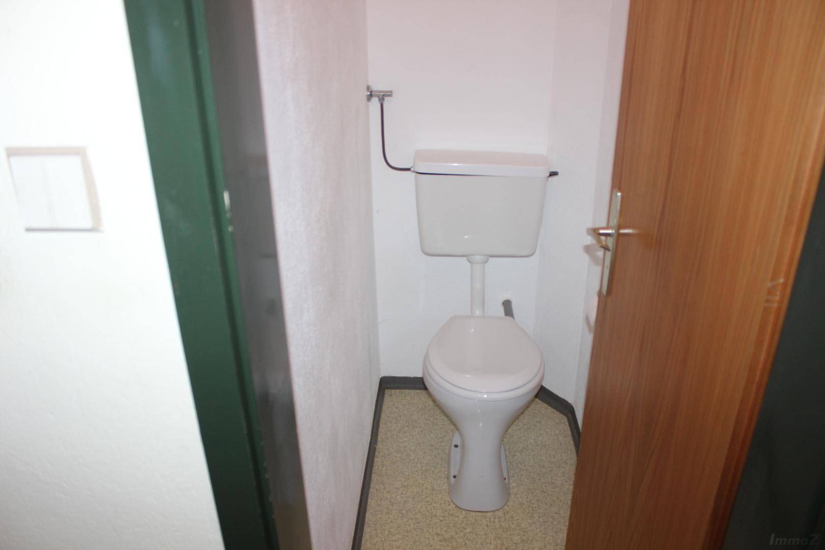 Kleines Gäste-WC mit einfacher Toilette und hellem Bodenbelag, praktisch und funktional.