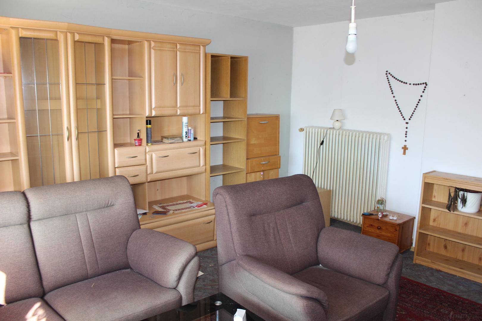 Wohnzimmer mit umfangreicher Holzschrankwand, bequemen Sofas und einem Heizkörper.