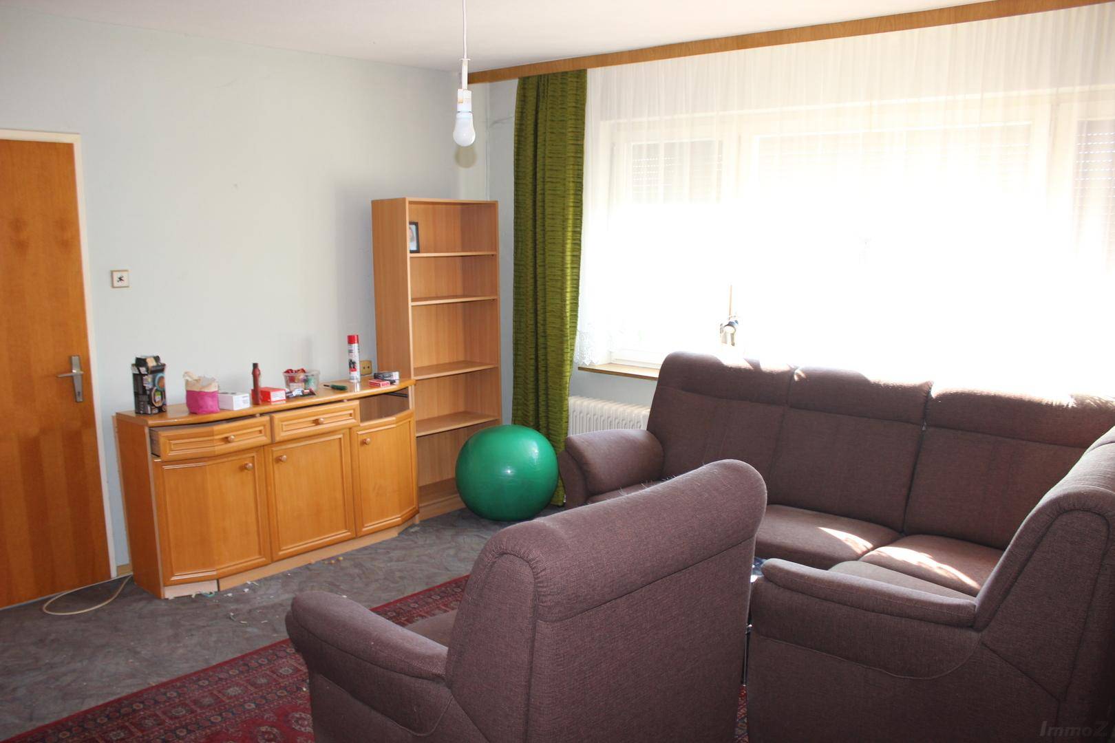 Wohnzimmer mit großem Fenster, das viel Tageslicht hereinlässt, und einem Holzschrank.