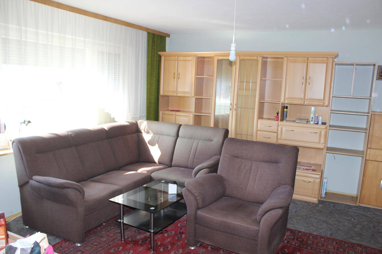 Gemütliches Wohnzimmer mit braunem Ecksofa, Glastisch und einer großen Holzschrankwand.
