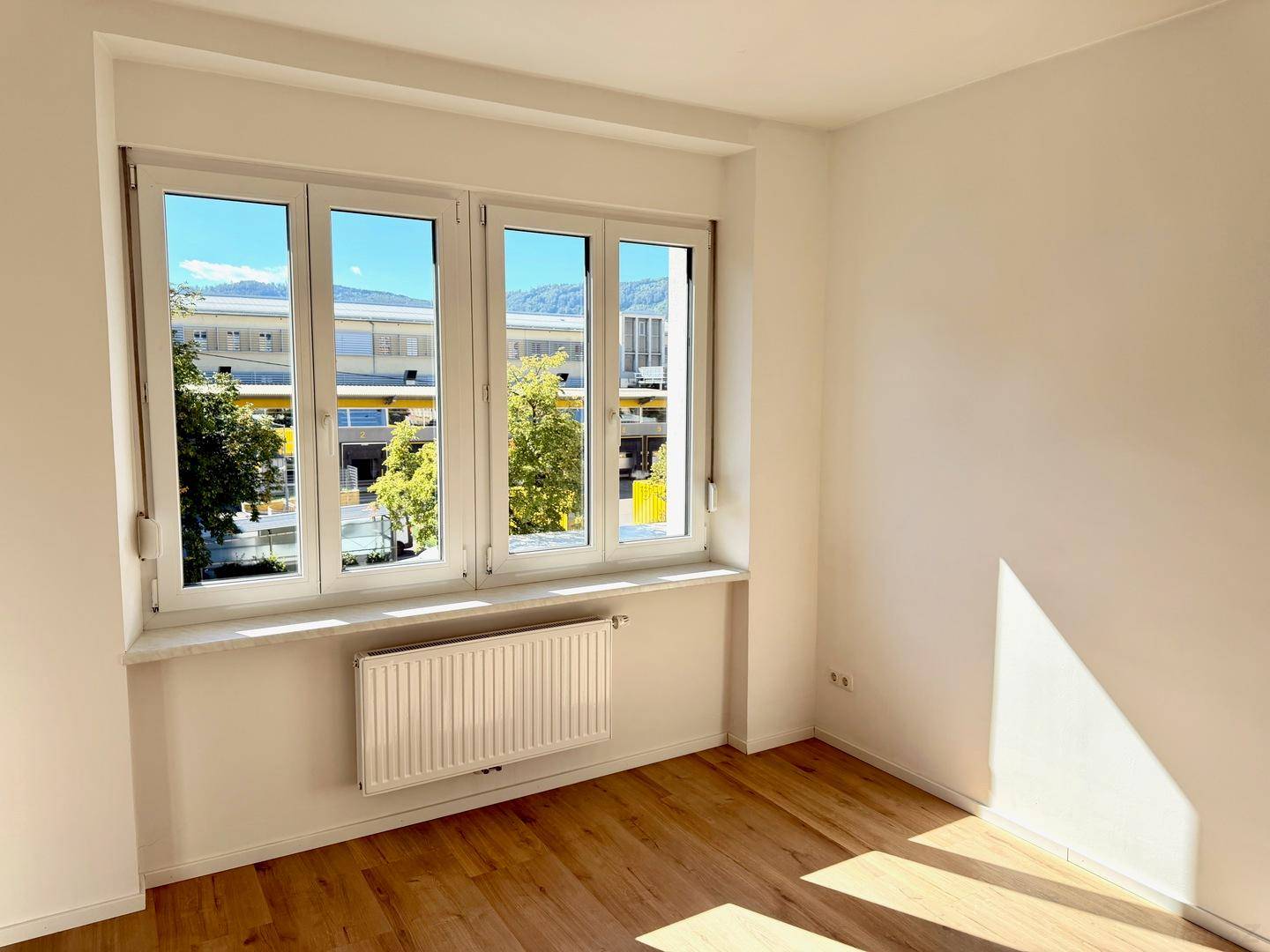 Helles Zimmer mit großem Fenster, Laminatboden und Blick auf die Umgebung.